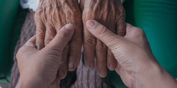 Mujer agarrando las manos de un anciano.
