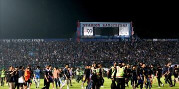 Aficionados ingresan al campo de un estadio luego de que su equipo perdiera un partido de fútbol mientras que los agentes de seguridad intentan dispersarlos en Malang, Java Oriental, Indonesia, el 1 de octubre de 2022.