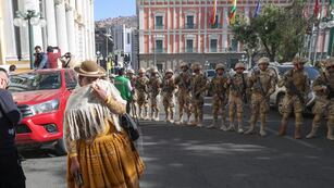 Una mujer pasa entre los militares formados frente a la sede del Gobierno de Bolivia, este miércoles en La Paz (Bolivia). El presidente Luis Arce dijo que el país "está atravesando un intento de golpe de Estado".