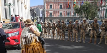 Una mujer pasa entre los militares formados frente a la sede del Gobierno de Bolivia, este miércoles en La Paz (Bolivia). El presidente Luis Arce dijo que el país "está atravesando un intento de golpe de Estado".