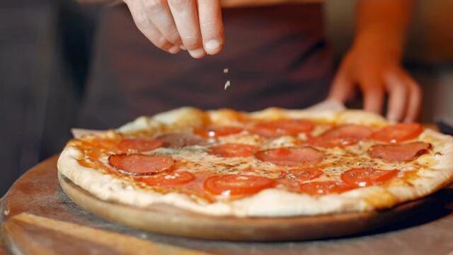 Mujer agregando toppings a una pizza.