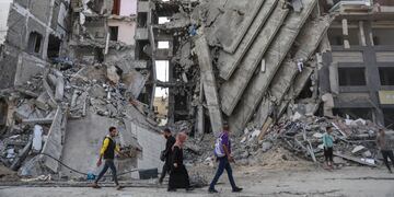 Palestinos caminan frente a edificios impactados por ataques israelíes en Ciudad de Gaza.