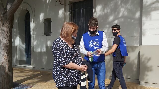 En la vereda del banco enseñando a los mayores a usar más frecuentemetne la tarjeta de débito para evitar estafas.