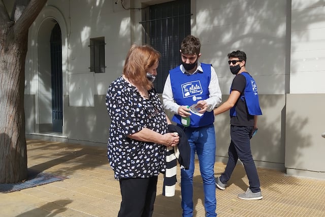 En la vereda del banco enseñando a los mayores a usar más frecuentemetne la tarjeta de débito para evitar estafas.