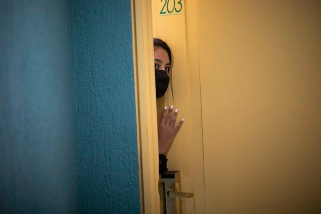Una paciente asintomática de COVID-19 se asoma desde la puerta de su habitación de hotel.