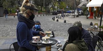 A waitress serves a table placed on a sidewalk in Buenos Aires, Argentina, on August 31, 2020, amid the COVID-19 coronavirus pandemic\u002E - Restaurants and bars reopened on Monday in the city of Buenos Aires after six months of lockdown with tables placed in open-air spaces\u002E (Photo by JUAN MABROMATA / AFP)