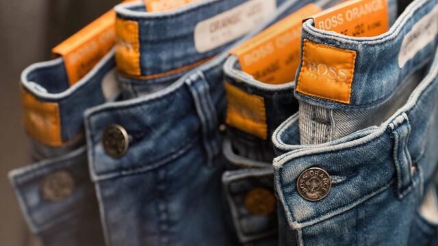 Tags sit stitched into the waistband of Boss Orange jeans as they hang on display at a Hugo Boss AG showroom in Metzingen, Germany, on Thursday, March 9, 2017. Hugo Boss AG, the ailing German clothier, said earnings may rise in 2017 as its turnaround takes shape after profit plummeted on weak sales in China and the U.S. last year. Photographer: Krisztian Bocsi/Bloomberg alemania  anuncio de la marca empresa Hugo Boss reestructuracion de la firma para aumentar las ventas caida de las ventas en el au00f1o 2016
