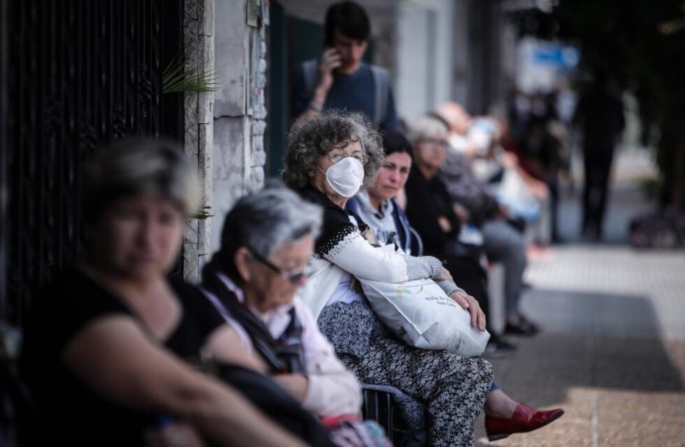 Los jubilados esperan la apertura de bancos, sentados, a distancia y tomando bebidas calientes
