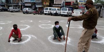En la ciudad de Jammu, un policía obliga a dos ciudadanos a permanecer en cuclillas, como castigo por romper la cuarentena\u002E (Jaipal Singgh/EFE)\u002E