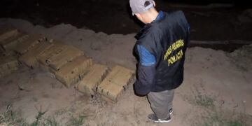 Un agente del Departamento de Drogas Peligrosas de la provincia de Chaco observa los bultos encontrados en la costa\u002E