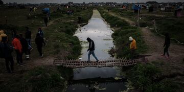 AME5908\u002E GUERNICA (ARGENTINA), 18/09/2020\u002E- Personas cruzan un arroyo por un puente improvisado, el 15 de septiembre de 2020, en la toma de tierras de la localidad de Guernica, a 30 km de Buenos Aires (Argentina)\u002E Más de mil personas en condición de pobreza se instalaron desde el 20 de julio en un terreno de 100 hectáreas ubicado en Guernica, conformando la más grande toma de tierras en la provincia de Buenos Aires\u002E EFE/ Juan Ignacio Roncoroni