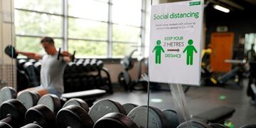A sign displaying the rules about remaining at a safe distance are attached to a mirror in the gymnasium at Nuffield Health Sunbury Fitness and Wellbeing Gym in Sunbury-on-Thames, west of London on July 25, 2020 as novel coronavirus lockdown restrictions are eased to allow gyms, leisure centres and indoor swimming pools in England to reopen\u002E - England's gyms, leisure centres and indoor swimming pools were allowed to open their doors on July 25 for the first time since the March shutdown was introduced to combat the novel coronavirus COVID-19 pandemic\u002E (Photo by ADRIAN DENNIS / AFP)