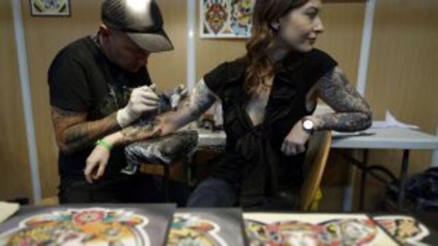 A tattooist works on a woman's arm during the first day of the second