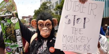En esta foto de archivo tomada el 8 de mayo de 2019, un hombre con una máscara de mono sostiene un cartel mientras la gente bloquea la calle en una protesta contra Uber y Lyft\u002E Crédito: Josh Edelson / AFP\u002E