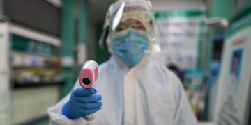 TOPSHOT - A medical worker prepares to check the temperature of an AFP photojournalist before a COVID-19 coronavirus test in Wuhan in China's central Hubei province on April 16, 2020\u002E - China has largely brought the coronavirus under control within its borders since the outbreak first emerged in the city of Wuhan late last year\u002E (Photo by Hector RETAMAL / AFP)