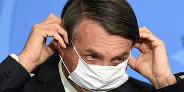 Brazilian President Jair Bolsonaro puts on a facemask during the signing ceremony of a new decree that facilitates access to credit for small business and fights the economic impacts resulting from the pandemic of the novel coronavirus, at Planalto Palace in Brasilia, on August 19, 2020\u002E (Photo by EVARISTO SA / AFP)