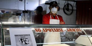 A man wearing a mask waits for clients at his shop, with a sign posted that reads in Spanish \