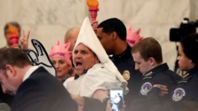 A protestor is escorted away by Capitol Hill Police officers, Tuesday, Jan. 10, 2017, in Washington, during the Senate Judiciary Committee's confirmation hearing for Attorney General-designate, Sen. Jeff Sessions, R-Ala. (AP Photo/Alex Brandon)