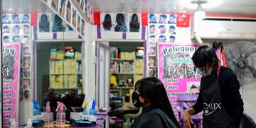 A hairdresser cuts the hair of a customer, both wearing face masks as a preventive measure against the novel coronavirus, COVID-19, at a hairdresser in Villa 31 shantytown in downtown Buenos Aires, on May 5, 2020\u002E - Villa 31, the oldest shantytown in Buenos Aires, is separated only by an avenue from exclusive neighbourhoods of the capital\u002E Crowded, hungry and suffering water services faults, residents of the slum now face the menace of COVID-19\u002E (Photo by Ronaldo SCHEMIDT / AFP)