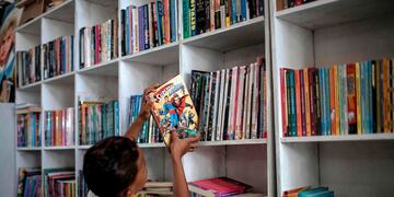 A boy places a book on a shelve of the public library Mundo da Lua (Lua's World), founded by Brazilian 12-year-old Lua Oliveira five months ago, at the Tabajaras favela in Rio de Janeiro, Brazil, on March 10, 2020\u002E - Lua had the idea to open a public library after visiting the Rio de Janeiro International Book Fair last year and made posts in social networks asking for donations, which went viral\u002E (Photo by MAURO PIMENTEL / AFP)