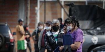 Personas usan tapabocas hoy mientras hacen fila para obtener alimentos en un comedor comunitario, en una villa de la Ciudad de Buenos Aires (EFE/JUAN IGNACIO RONCORONI)