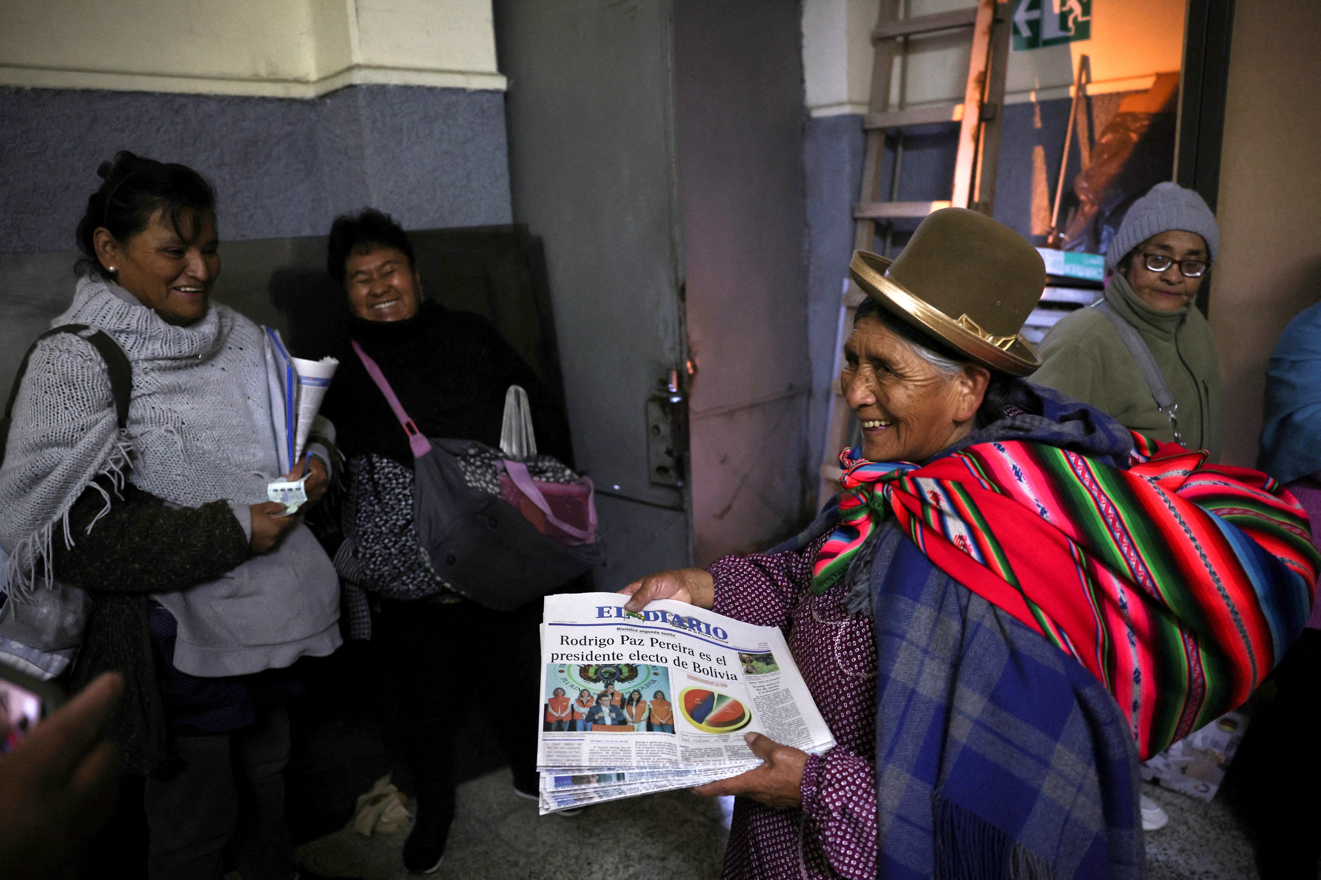 Una vendedora de diarios entrega a sus clientes ejemplares con la cobertura en primera plana de la segunda vuelta presidencial de Bolivia, que ganó Rodrigo Paz para suceder al presidente saliente Luis Arce, del Movimiento al Socialismo (MAS).