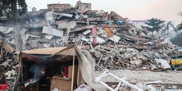 Personas se protegen en una tienda de campaña cerca de un edificio derrumbado tras un fuerte terremoto en Hatay, Turquía.