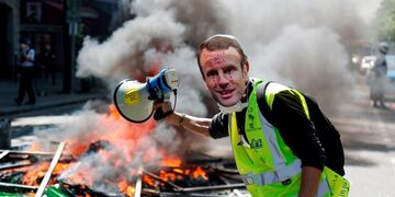 TOPSHOT - A protester wearing a mask of French President Emmanuel Macron crying stands next to a burning barricade during an anti-government demonstration called by the 'Yellow Vests' (gilets jaunes) movement, on April 20, 2019 in Paris\u002E (Photo by Zakaria ABDELKAFI / AFP)