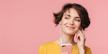 Image of a happy young beautiful woman posing isolated over pink wall background listening music with earphones using mobile phone\u002E
