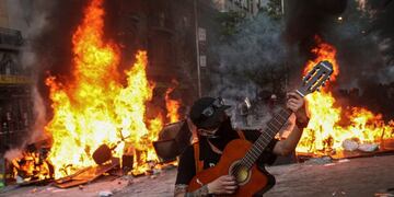 Un manifestante toca una guitarra frente a una barricada en llamas durante una protesta en Santiago, Chile, el martes 12 de noviembre de 2019\u002E Crédito: AP Photo/Esteban Felix\u002E