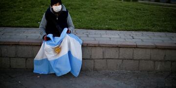 A woman, holding an Argentine national flag, sits on a stone ledge wall during a protest against a wide range of issues including government economic policy and state policies to combat the spread of COVID-19, in Buenos Aires, Argentina, Saturday, Sept\u002E 19, 2020\u002E (AP Photo/Natacha Pisarenko)