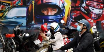 (FILES) In this file photo taken on March 2, 2020 a woman wearing a facemask checks her smartphone in front of a poster outside the Formula One Vietnam Grand Prix merchandise store in Hanoi\u002E - Vietnam's 2020 Formula One Grand Prix has been cancelled, organisers said on October 16, but there was no word on whether the race would take place next year\u002E (Photo by Nhac NGUYEN / AFP)