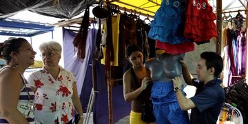 Unas posibles compradoras (izquierda) miran la ropa que venden Yeisker Castillo y su esposa Lisbet Tejeda (derecha), quienes visten un maniquu00ed en un puesto de un mercado al aire libre donde el gobierno permite que los comerciantes con licencia vendan sus