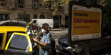 A taxi driver wearing a protective mask carries flowers next to a sign that reads \