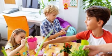 Coloring buckets\u002E Three cute pupils feeling busy and interested while looking cute while coloring buckets for plants