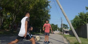 Dos chicos juegan a la pelota junto a un poste de madera inclinado. (José Hernández)