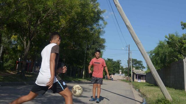 Dos chicos juegan a la pelota junto a un poste de madera inclinado. (José Hernández)
