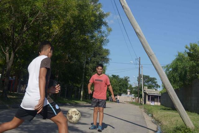 Dos chicos juegan a la pelota junto a un poste de madera inclinado. (José Hernández)