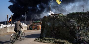 Ucrania. Un hombre anda en bicicleta mientras, de fondo, se levanta una columna de humo negra tras ataques rusos en las afueras de Kiev. (AP / Rodrigo Abd)