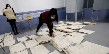 Trabajadores electorales con máscaras protectoras revisan y cuentan los votos después del cierre de las urnas.