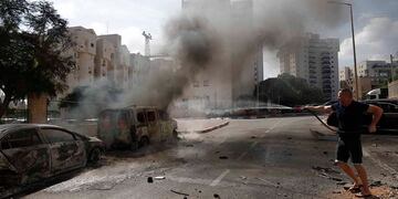 Un residente apaga vehículos en llamas en la ciudad israelí de Ashkelon tras el lanzamiento de cohetes desde Gaza, 7 de octubre de 2023. Foto: EFE