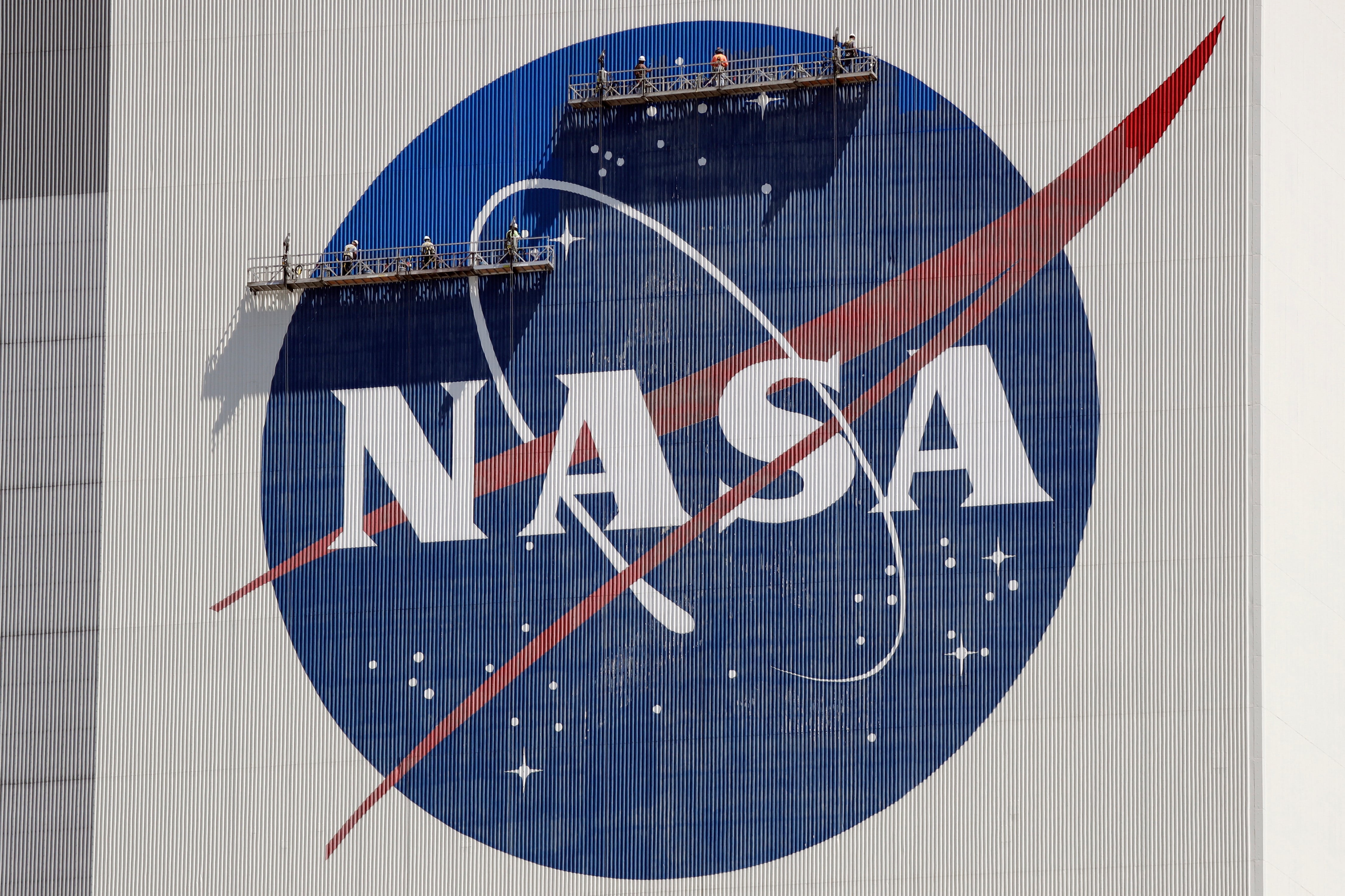 ARCHIVO - trabajadores en andamios repintan el logo de la NASA en el Centro Espacial Kennedy, Cabo Cañaveral, Florida, 20 de mayo de 2020. La NASA dijo el jueves 14 de setiembre de 2023 que el estudio de los OVNI requerirá nuevas técnicas científicas y satélites más avanzados, así como un cambio en la percepción de los objetos voladores no identificados. La agencia espacial dedicó un año al estudio de los OVNI antes de dar a conocer su informe. (AP Photo/John Raoux, File)