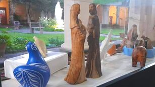Estilizadas imágenes talladas en madera que representan a María y José, junto a figuras de diversos estilos y diferentes materiales, en la muestra montada en los jardines del convento franciscano de Jujuy.