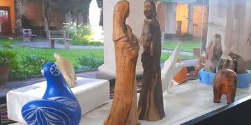Estilizadas imágenes talladas en madera que representan a María y José, junto a figuras de diversos estilos y diferentes materiales, en la muestra montada en los jardines del convento franciscano de Jujuy.